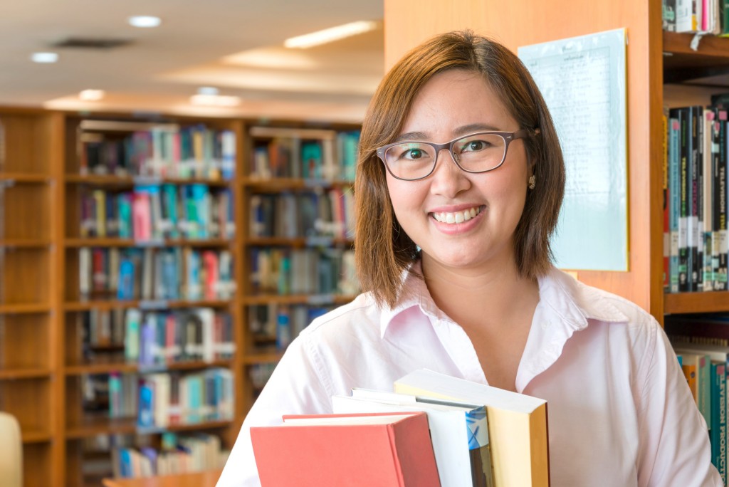 In the library - Aisian female student with books working in a university library.